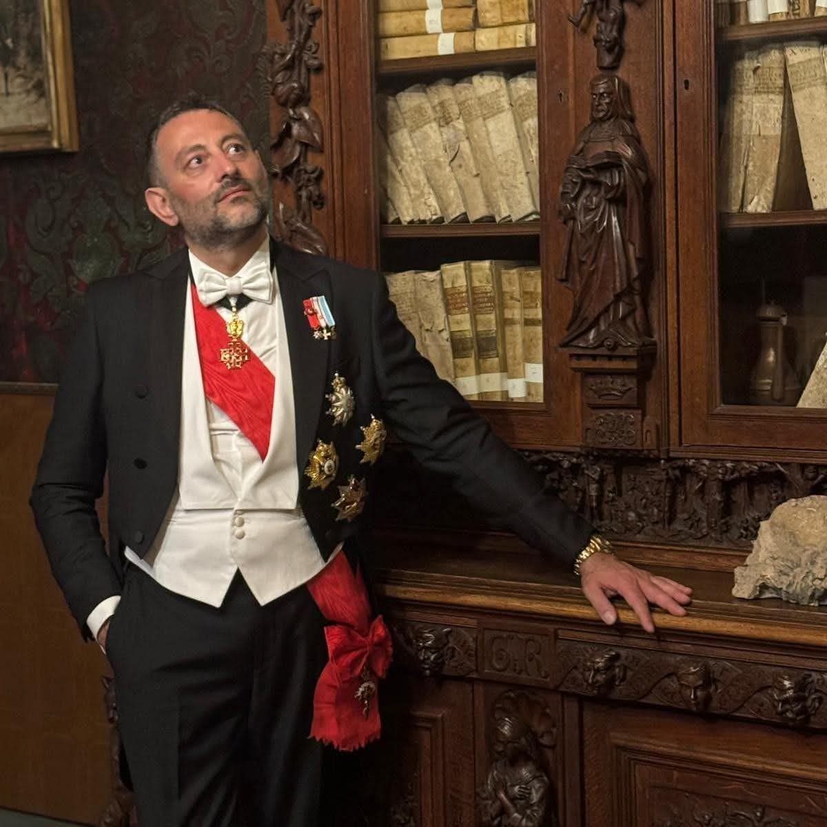 A member in white tie before a carved bookcase of old volumes