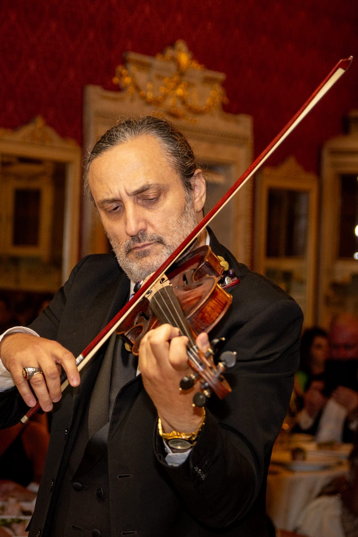 A violinist playing among the tables in a red damask salon
