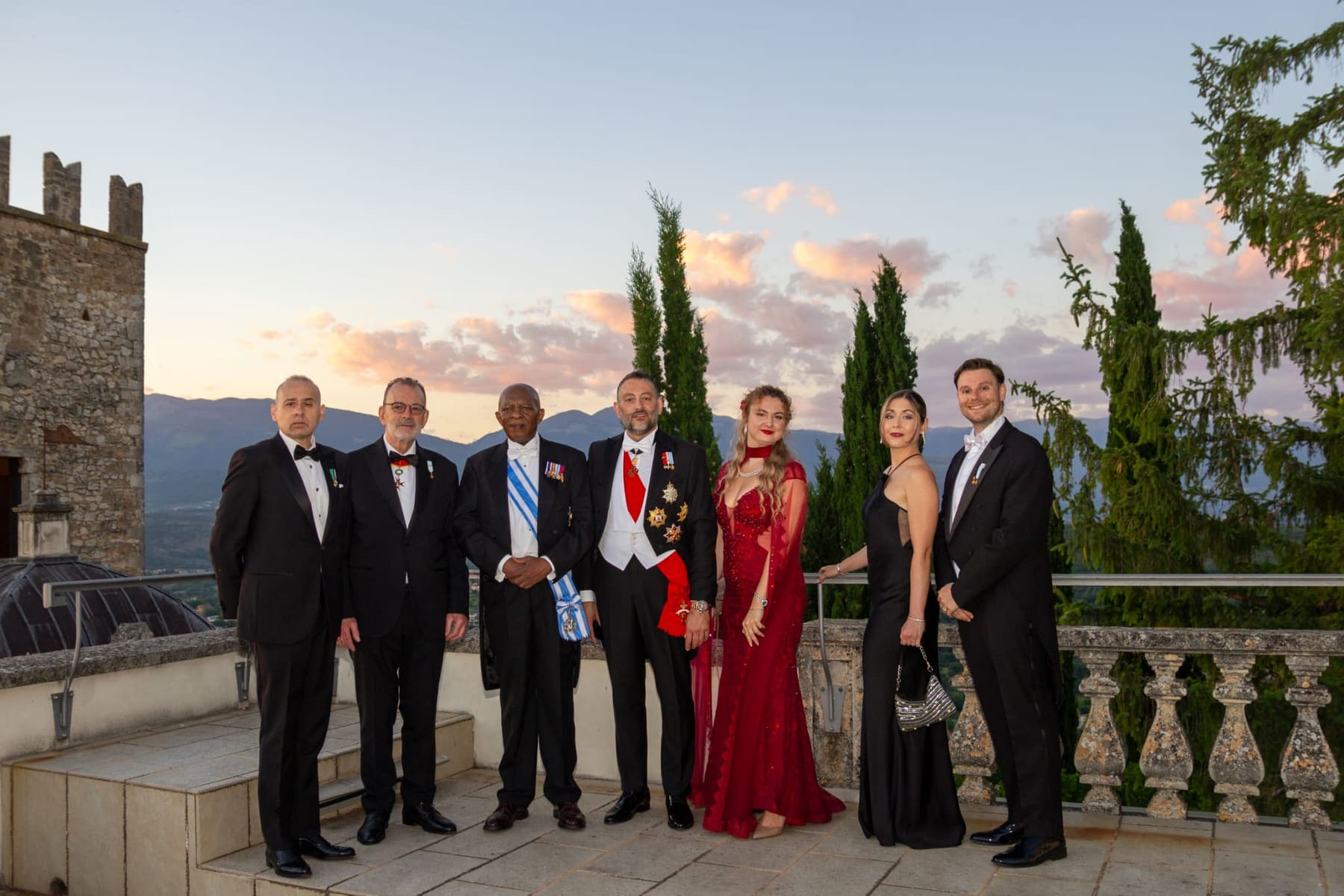 Members and guests on a stone terrace at sunset, cypresses behind